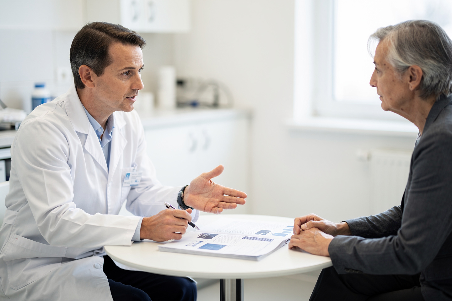 A doctor explains Pathology consultation before treatment to a patient reviewing medical papers.