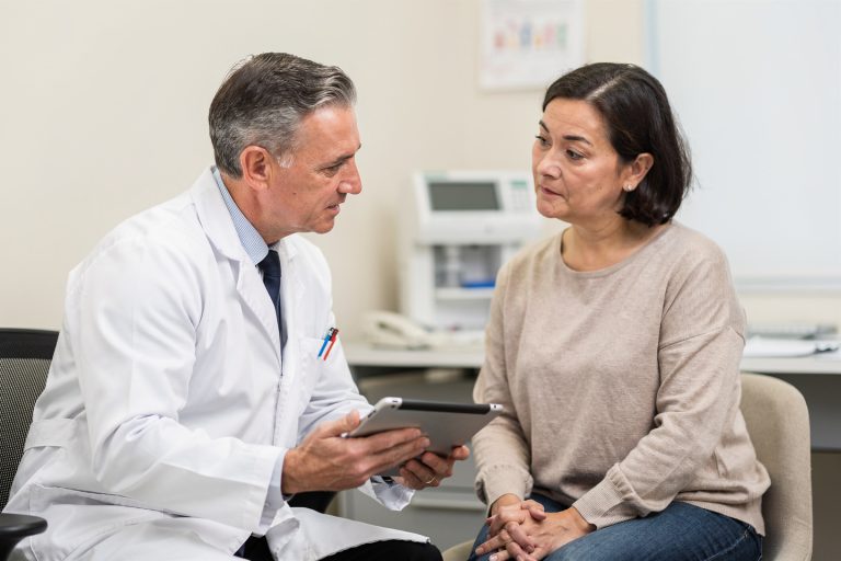 Doctor explaining pathology report treatment decisions to a patient in a calm consultation room.