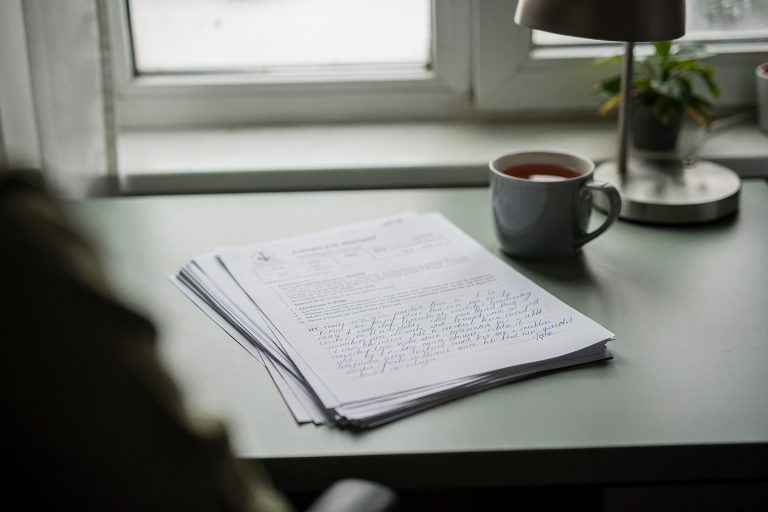A quiet home desk by a window with an autopsy report and notes, reflecting questions families ask after receiving an autopsy report.