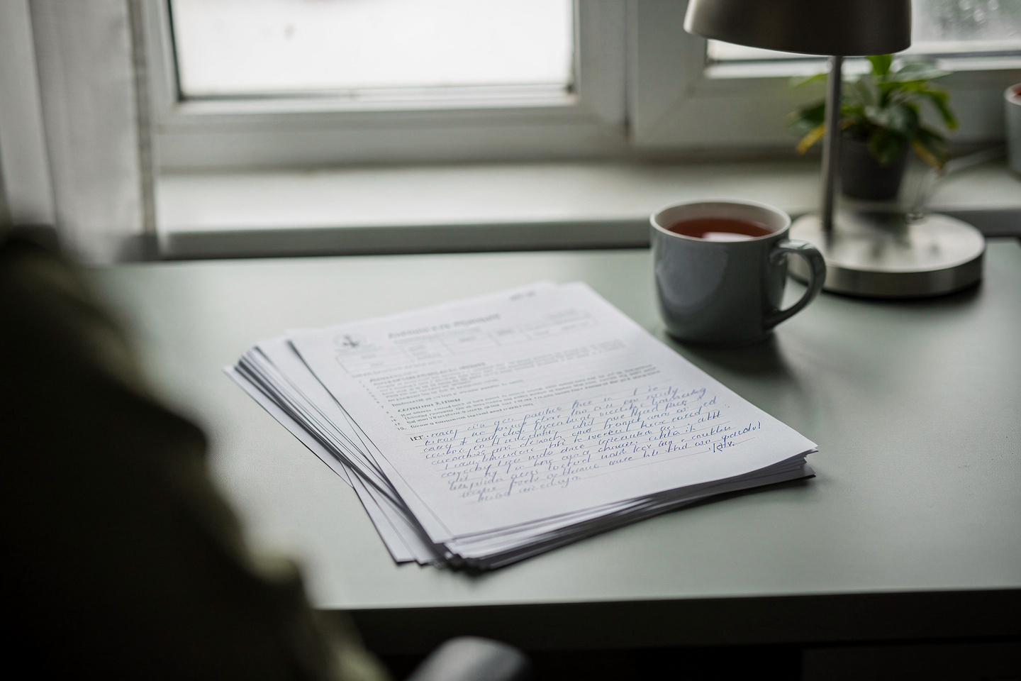 A quiet home desk by a window with an autopsy report and notes, reflecting questions families ask after receiving an autopsy report.