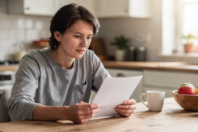 Person reading a letter at a kitchen table while considering a cancer pathology consultation after a diagnosis