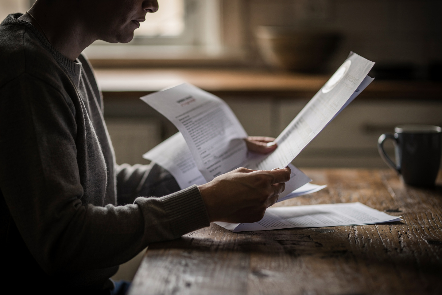 A person reads a pathology report at a kitchen table, reflecting how pathology reports influence treatment decisions, surgery, and prognosis.