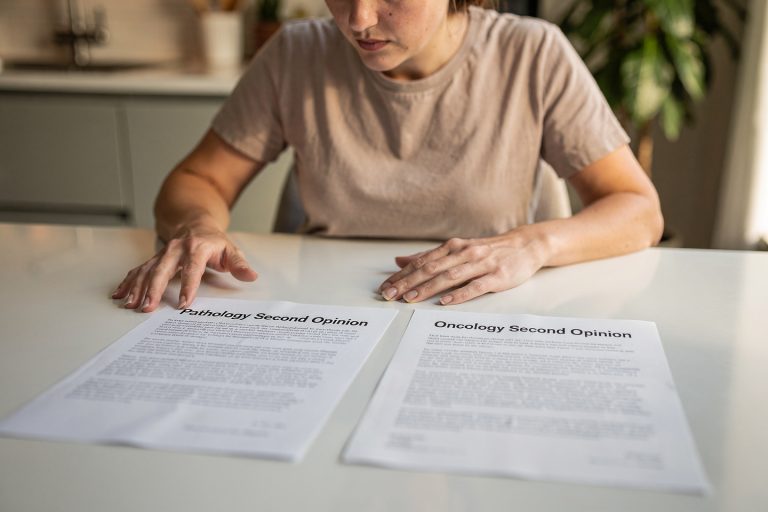 Person at a kitchen table comparing medical letters for a pathology second opinion versus an oncology second opinion.